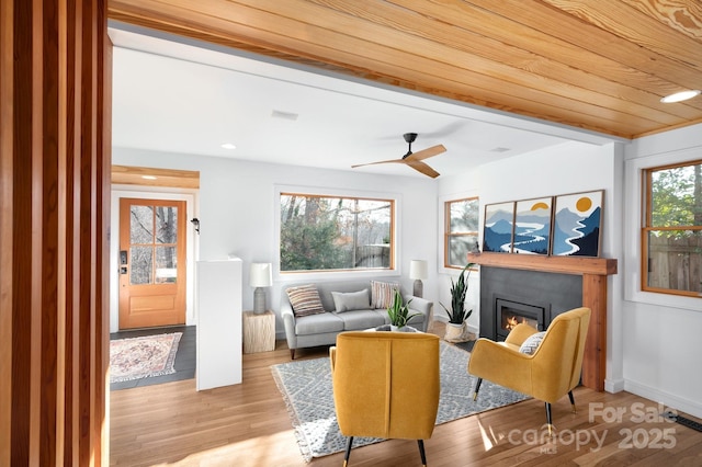 living area with a ceiling fan, a glass covered fireplace, wood finished floors, baseboards, and wood ceiling