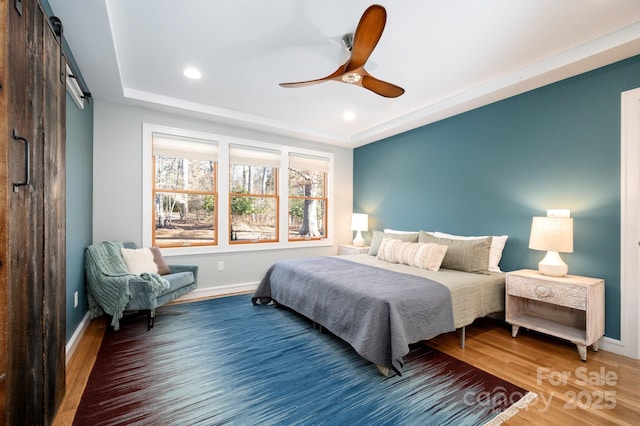 bedroom with wood finished floors, baseboards, recessed lighting, ceiling fan, and a barn door