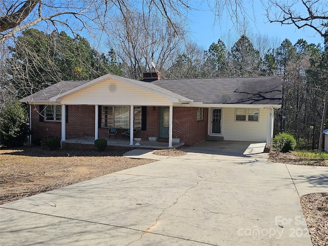 ranch-style home featuring brick siding, covered porch, concrete driveway, and a chimney