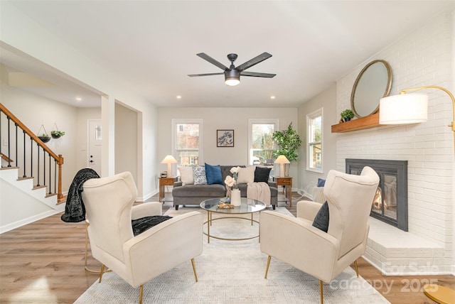 living area with a brick fireplace, baseboards, stairs, light wood-type flooring, and recessed lighting