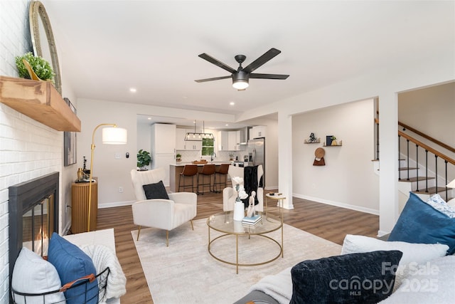 living room featuring a brick fireplace, baseboards, stairs, recessed lighting, and wood finished floors