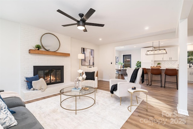 living area with light wood finished floors, recessed lighting, and a brick fireplace