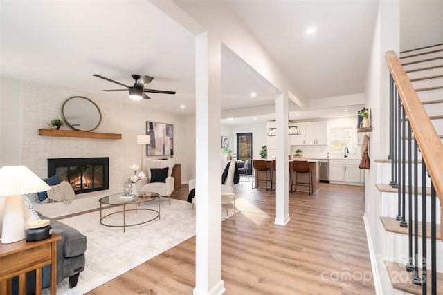 living room with recessed lighting, light wood-style floors, a brick fireplace, ceiling fan, and stairs