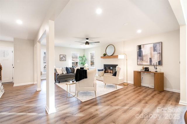 living room featuring light wood-style flooring, a brick fireplace, a ceiling fan, and baseboards