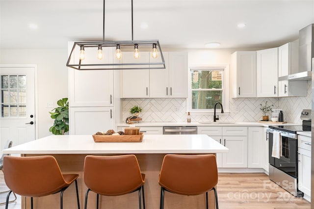 kitchen with a sink, stainless steel appliances, light countertops, a kitchen bar, and wall chimney exhaust hood