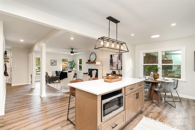 kitchen with light wood-style flooring, stainless steel microwave, a kitchen island, a fireplace, and a healthy amount of sunlight