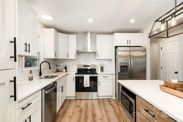 kitchen with light wood finished floors, light countertops, appliances with stainless steel finishes, wall chimney exhaust hood, and a sink