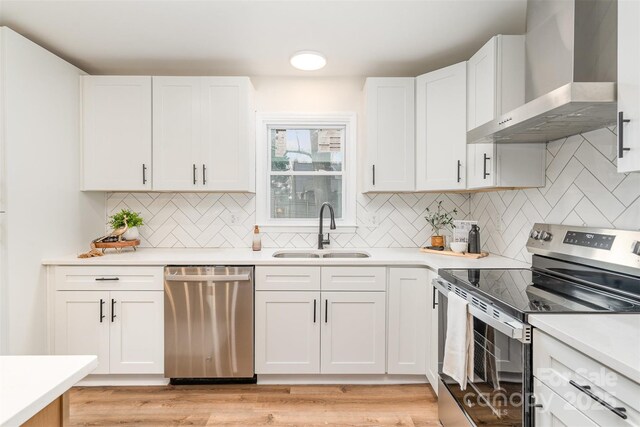 kitchen featuring a sink, light countertops, white cabinets, appliances with stainless steel finishes, and wall chimney exhaust hood