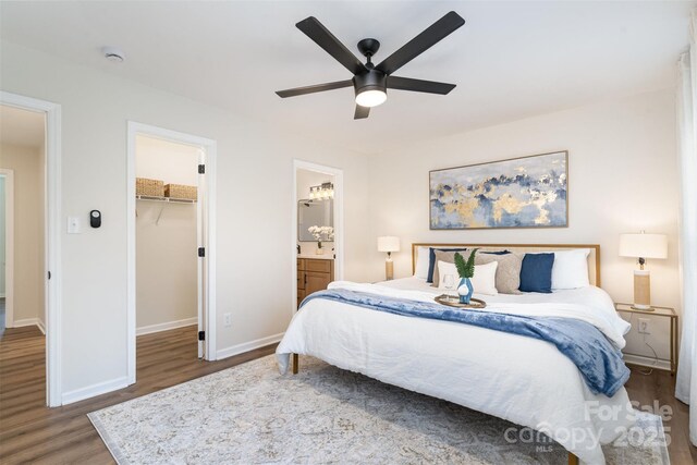 bedroom featuring a ceiling fan, ensuite bath, wood finished floors, baseboards, and a spacious closet