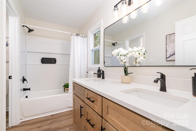 bathroom with wood finished floors, shower / bathtub combination with curtain, double vanity, and a sink