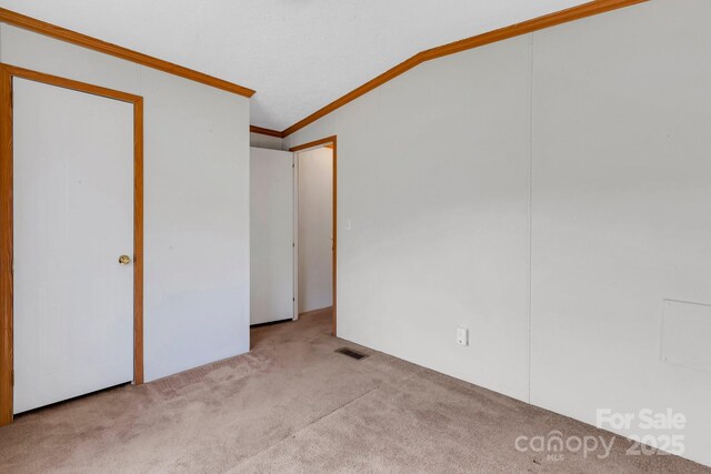 unfurnished bedroom with visible vents, crown molding, lofted ceiling, carpet floors, and a closet