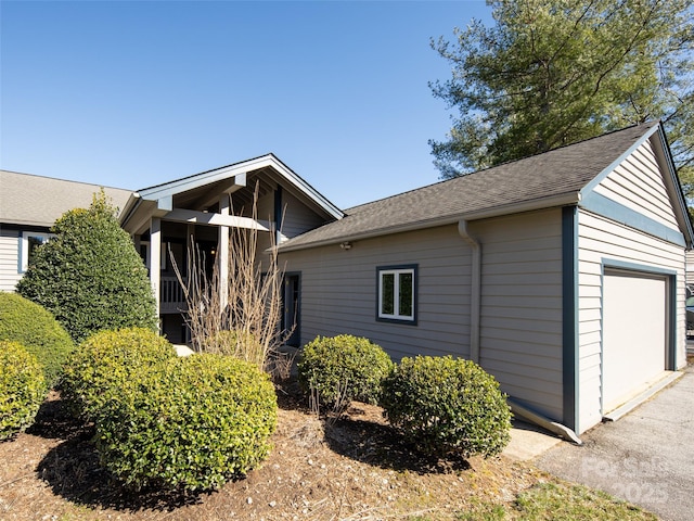 view of side of home featuring a garage and a shingled roof