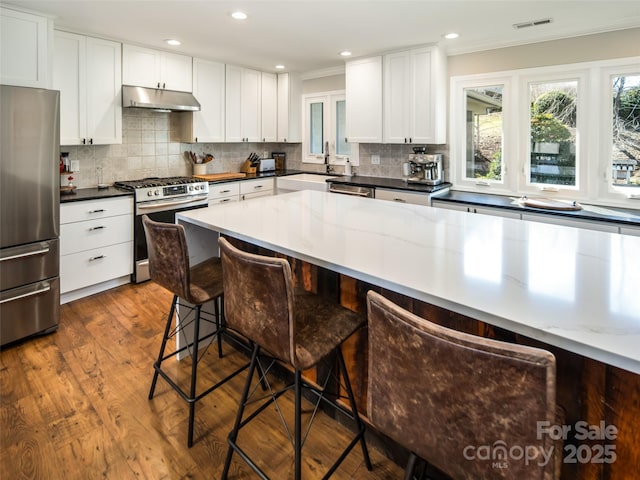 kitchen with visible vents, a breakfast bar, a sink, stainless steel appliances, and under cabinet range hood