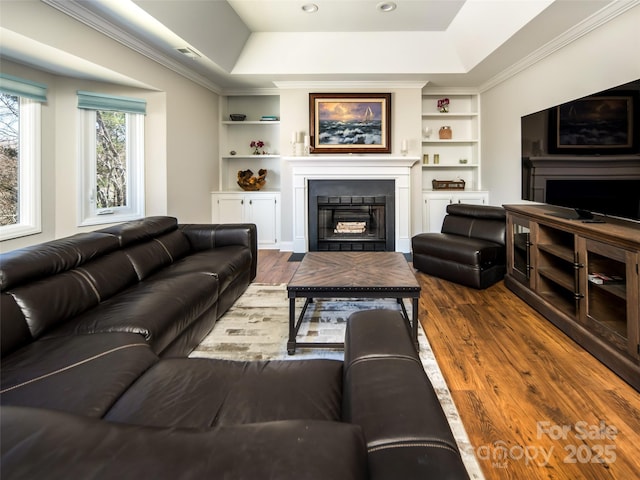 living room featuring a raised ceiling, a glass covered fireplace, and dark wood-style flooring