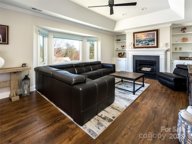 living room featuring hardwood / wood-style floors, a tray ceiling, built in features, and visible vents