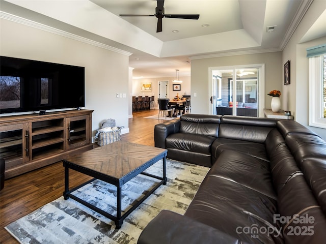 living room with visible vents, ornamental molding, a tray ceiling, and wood finished floors