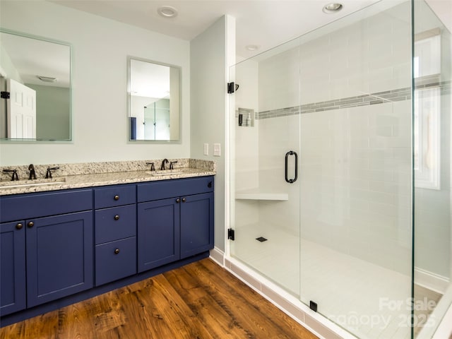 full bathroom with a sink, double vanity, wood finished floors, and a shower stall