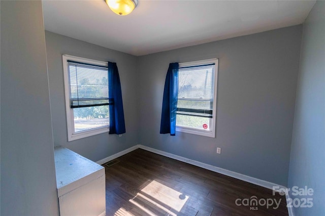 unfurnished room with visible vents, baseboards, and dark wood-style flooring