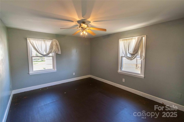 spare room featuring dark wood-style floors, visible vents, ceiling fan, and baseboards