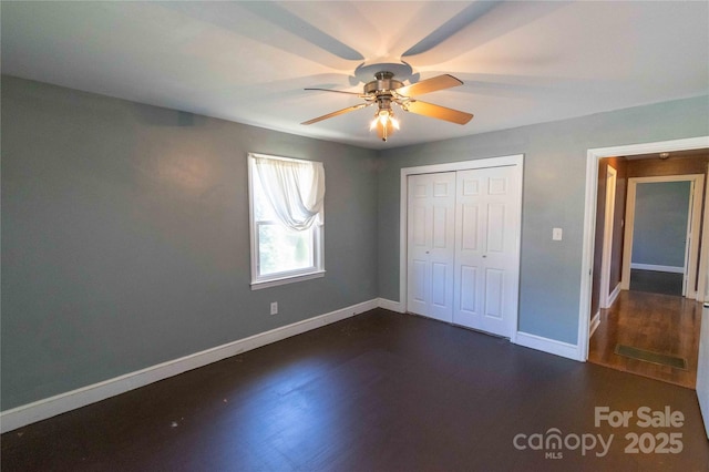 unfurnished bedroom featuring a closet, baseboards, ceiling fan, and dark wood-style flooring