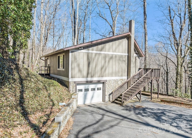 662 Locust Dr, Maggie Valley, NC 28751 - view of side of home with board and batten siding, asphalt driveway, an attached garage, a chimney, and stairway