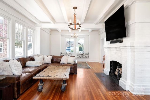 living area featuring beam ceiling, a brick fireplace, an inviting chandelier, and wood-type flooring