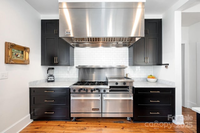 kitchen with backsplash, double oven range, wall chimney exhaust hood, and dark cabinets