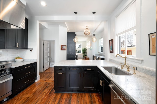 kitchen with a sink, dark cabinetry, dark wood finished floors, wall chimney range hood, and decorative backsplash