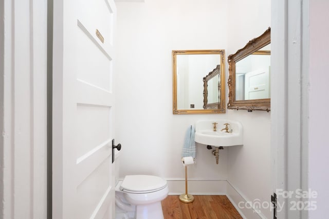 half bath featuring wood finished floors, toilet, baseboards, and a sink