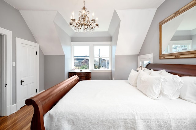 bedroom with lofted ceiling, an inviting chandelier, and wood finished floors