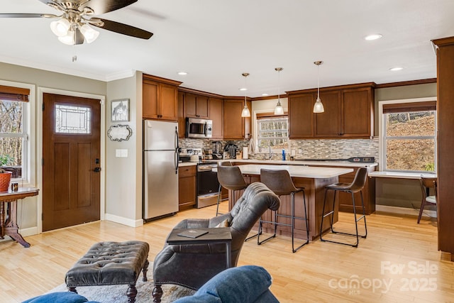 kitchen with open floor plan, light wood-style floors, appliances with stainless steel finishes, a breakfast bar area, and light countertops