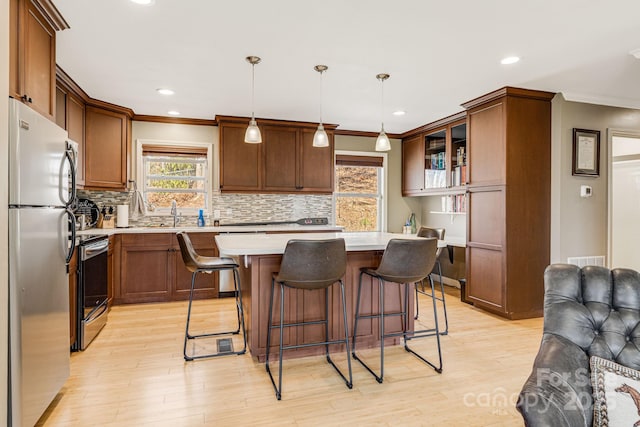 kitchen featuring a breakfast bar, open floor plan, stainless steel appliances, light wood-style floors, and light countertops