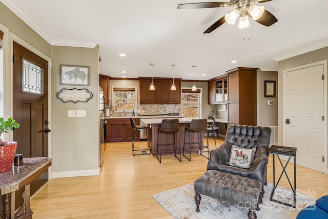 living area with a ceiling fan, baseboards, light wood-style flooring, recessed lighting, and ornamental molding