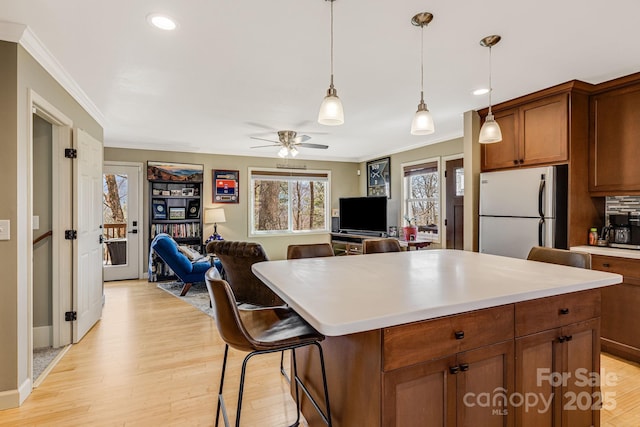 kitchen with light wood finished floors, open floor plan, light countertops, ornamental molding, and freestanding refrigerator