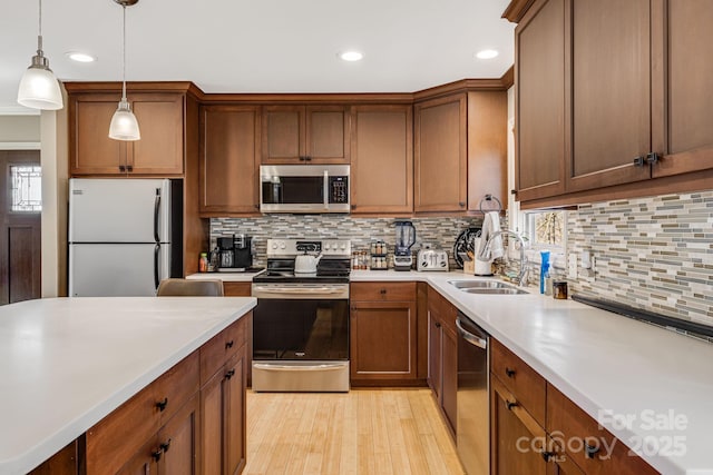 kitchen featuring light countertops, decorative backsplash, hanging light fixtures, stainless steel appliances, and a sink