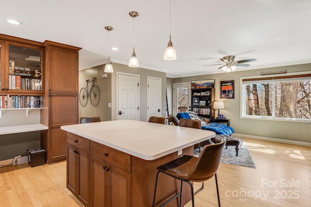 kitchen featuring light wood finished floors, a center island, light countertops, ornamental molding, and hanging light fixtures