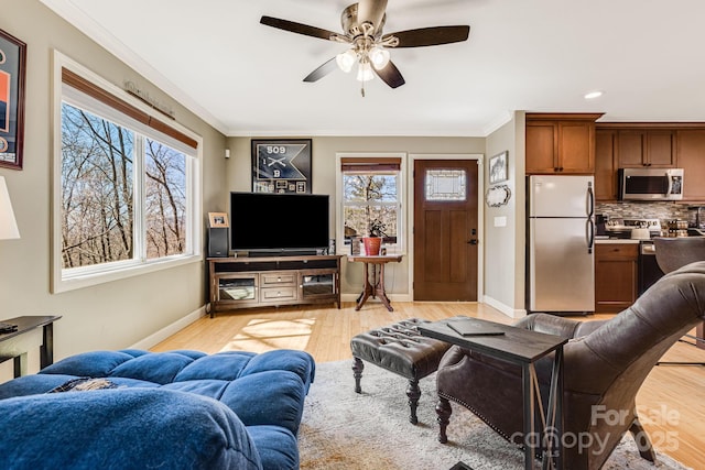 living room with ceiling fan, light wood-style floors, baseboards, and ornamental molding