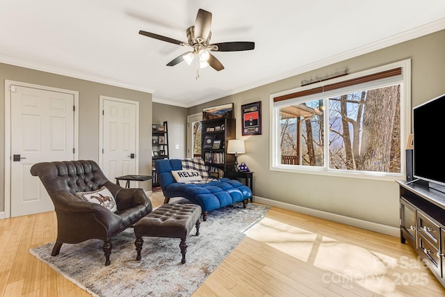 living room featuring light wood-style flooring, a ceiling fan, baseboards, and ornamental molding