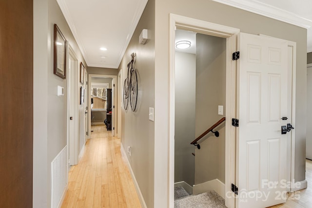 hall with visible vents, light wood-type flooring, baseboards, and ornamental molding