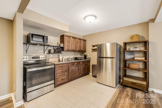 kitchen with open shelves, a sink, appliances with stainless steel finishes, light countertops, and baseboards