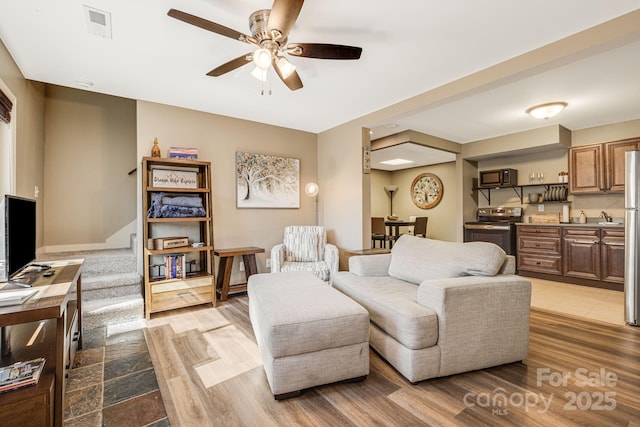 living room with light wood-type flooring, visible vents, and ceiling fan