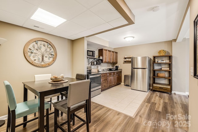 dining room featuring light wood-type flooring, visible vents, a paneled ceiling, and baseboards