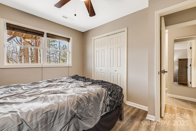 bedroom with light wood finished floors, visible vents, baseboards, a closet, and a ceiling fan