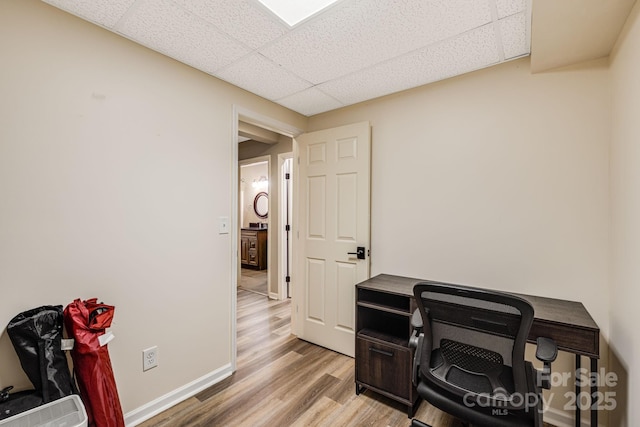 office featuring baseboards, a paneled ceiling, and light wood-style floors