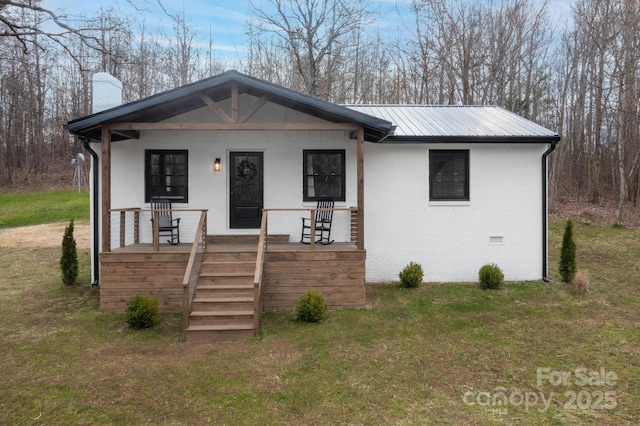 view of front facade with brick siding, a front yard, covered porch, a chimney, and metal roof