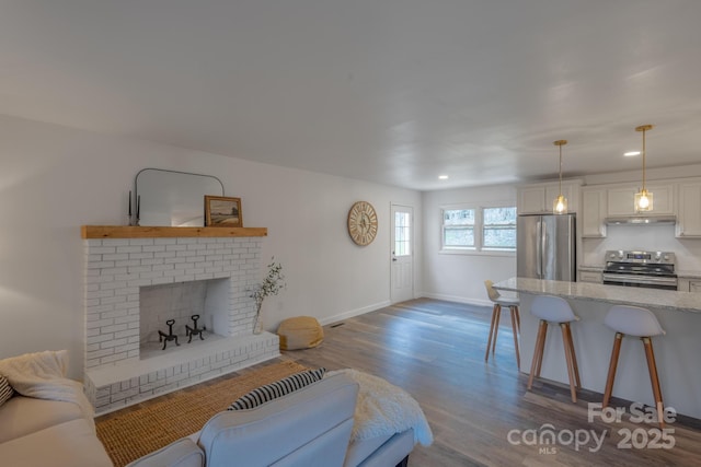 living room with dark wood finished floors, a brick fireplace, recessed lighting, and baseboards