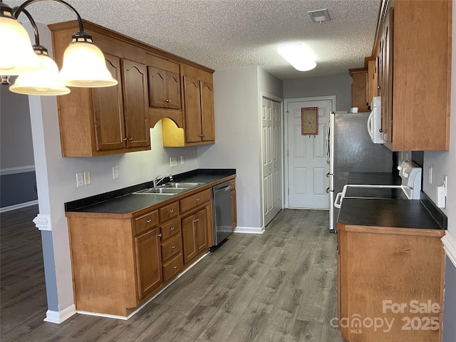 kitchen with dark countertops, visible vents, white microwave, stainless steel dishwasher, and a sink