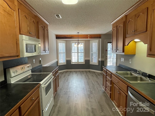 kitchen featuring white appliances, visible vents, a sink, dark countertops, and brown cabinets