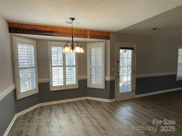 unfurnished dining area featuring an inviting chandelier, plenty of natural light, wood finished floors, and a textured ceiling