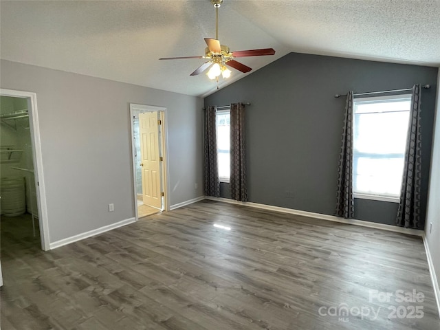 unfurnished bedroom featuring a textured ceiling, ensuite bath, wood finished floors, baseboards, and vaulted ceiling